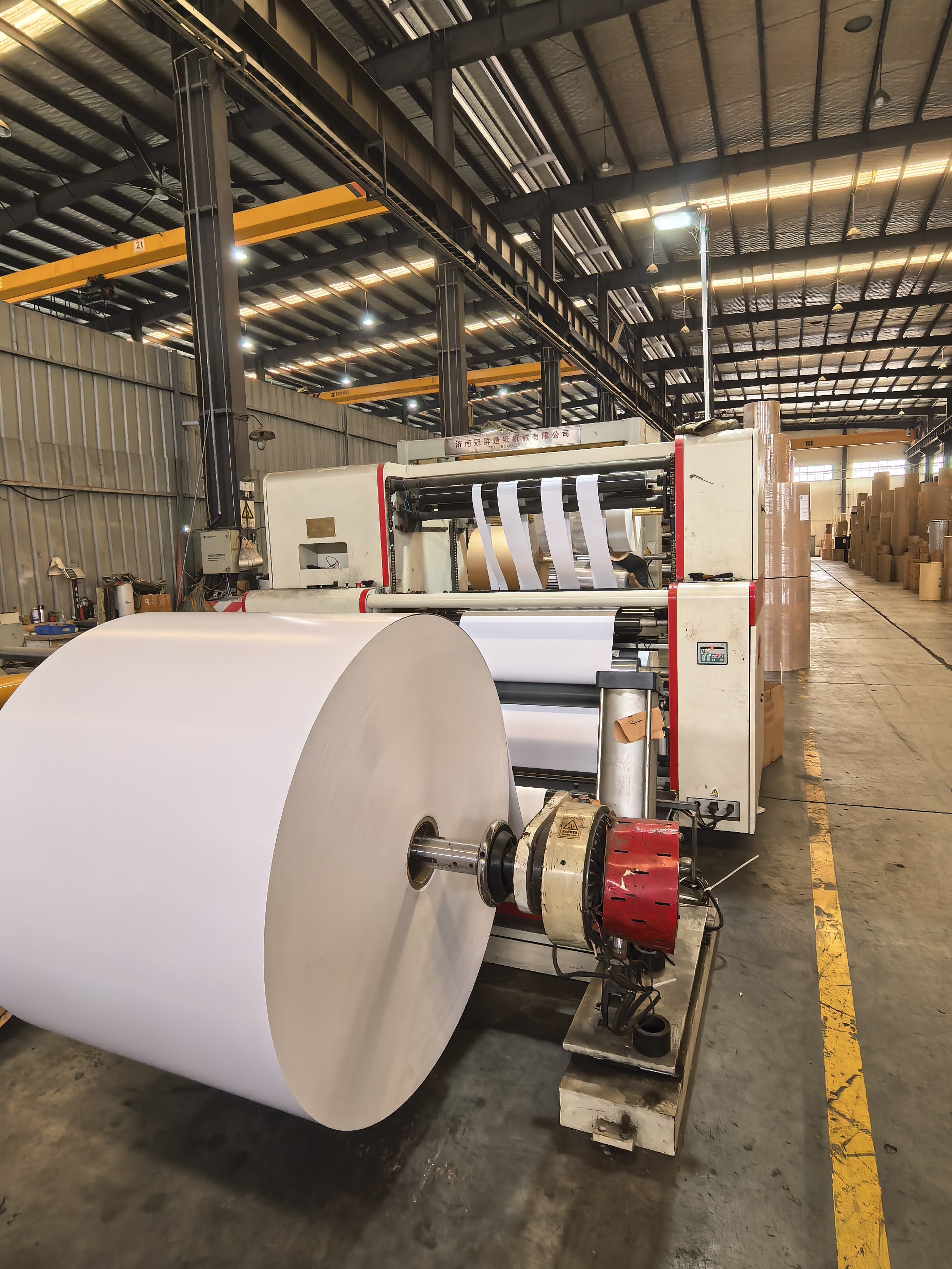 Slitting and rewinding machine with a large white paper roll in the foreground